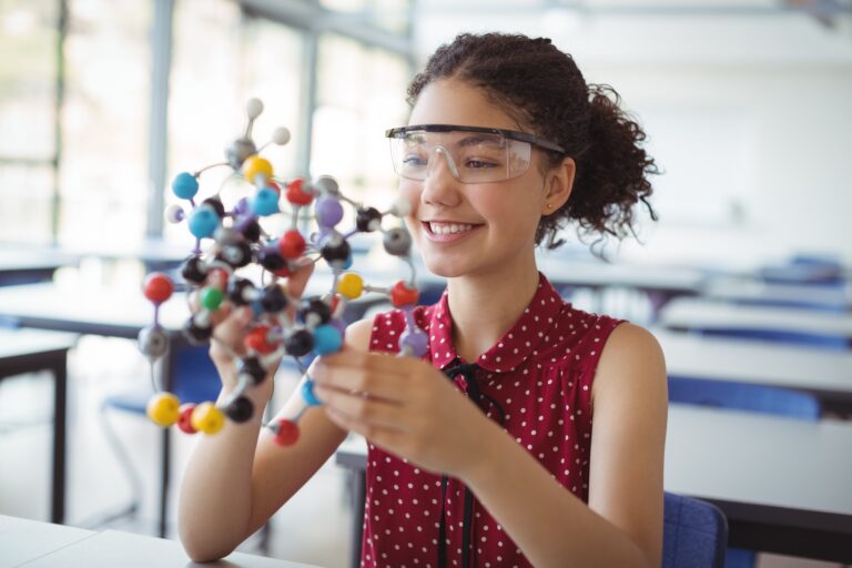 Happy schoolgirl holding experimenting model in laboratory