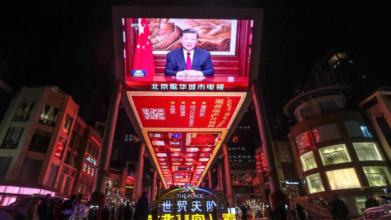 Chinese President, Xi Jinping, appears onscreen at the the Place shopping mall in Beijing, China. It is evening and the brightly lit screen is surrounded by lights from other buildings.